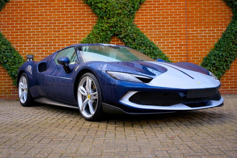 Sleek blue Ferrari sports car parked next to a brick wall with ivy, showcasing modern design and speed.