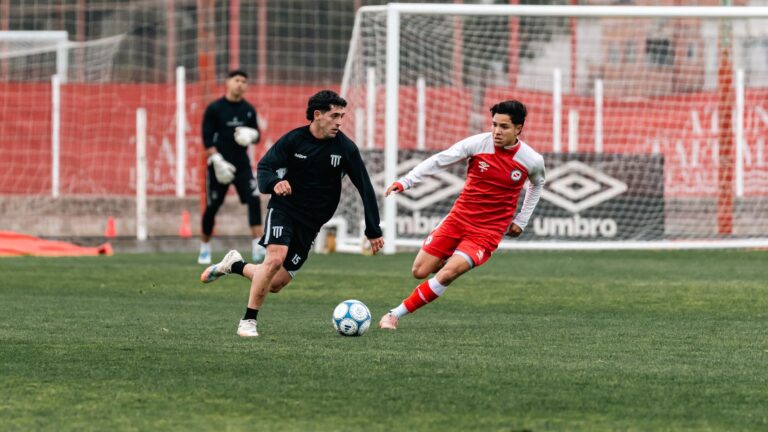 Two soccer players engage in an intense match with a goalkeeper in the background.
