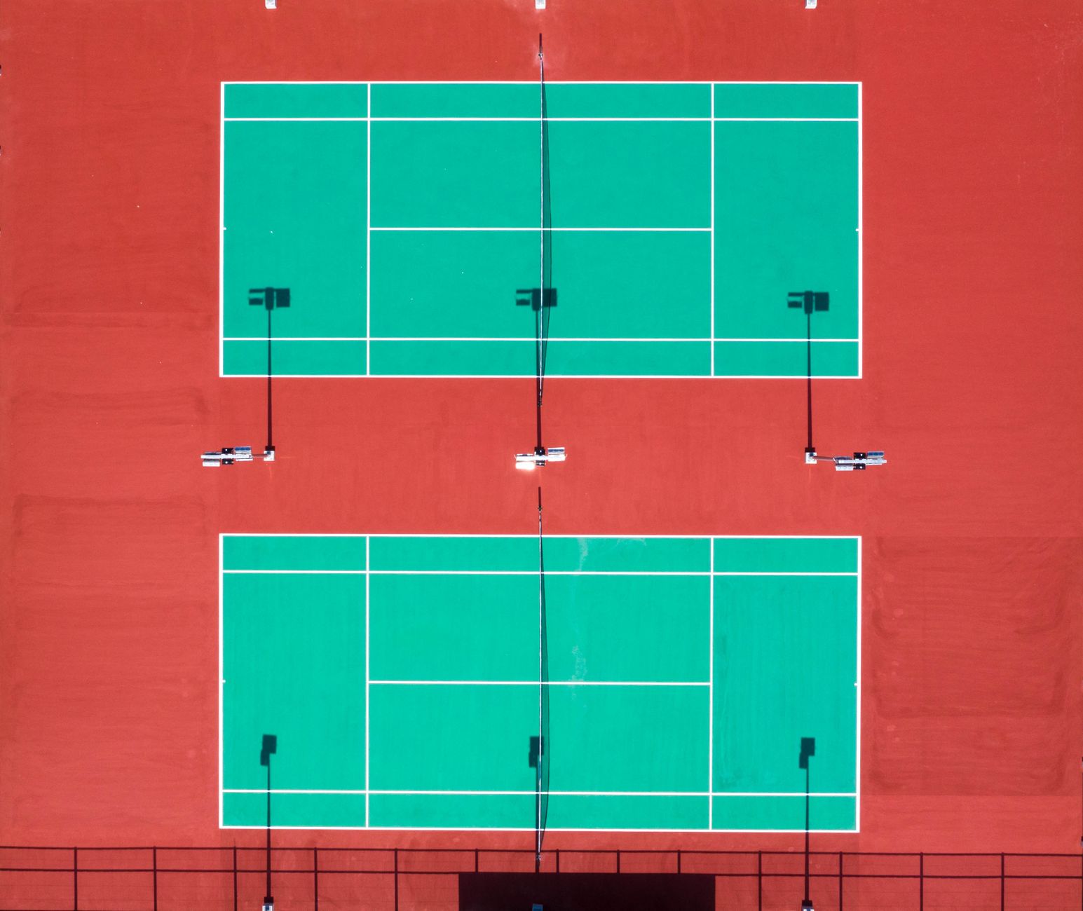 Bright aerial shot of two tennis courts on a sunny day.