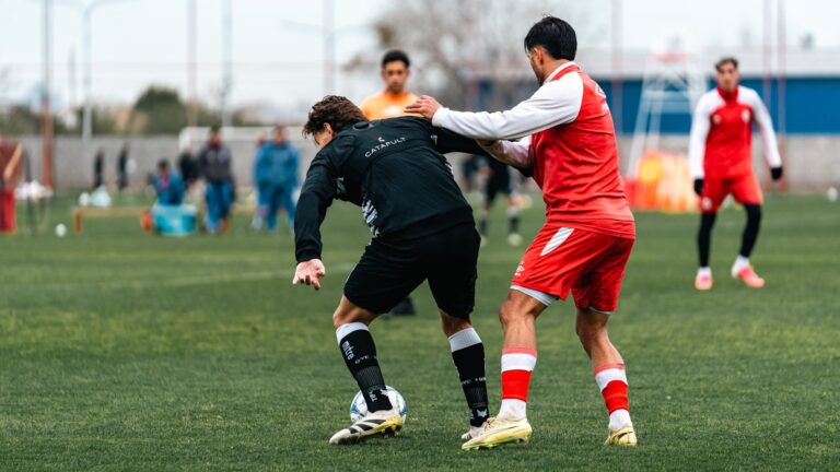 Action-packed soccer match with players in red and black jerseys competing on a green field.