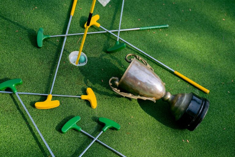 Colorful mini golf putters with a trophy on vibrant green turf, symbolizing victory.