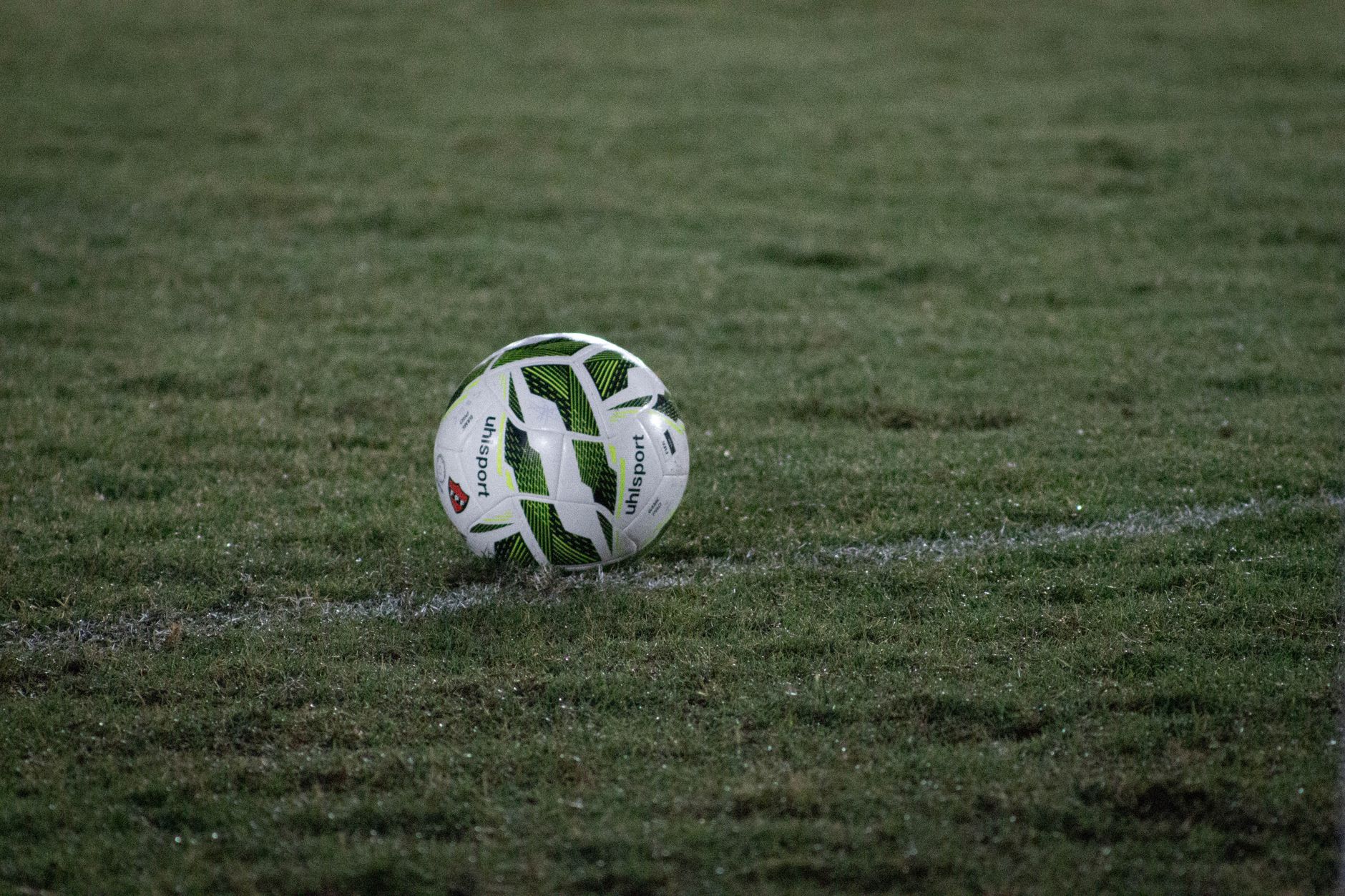 A soccer ball resting on a grass field, captured during nightfall with visible dew.