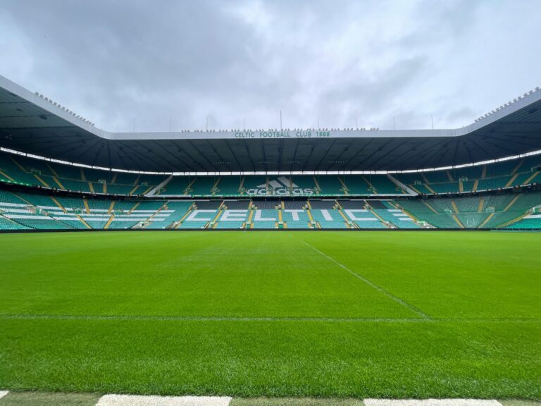 Wide-angle shot of the iconic Celtic Park stadium under a cloudy sky, showcasing its lush green field.