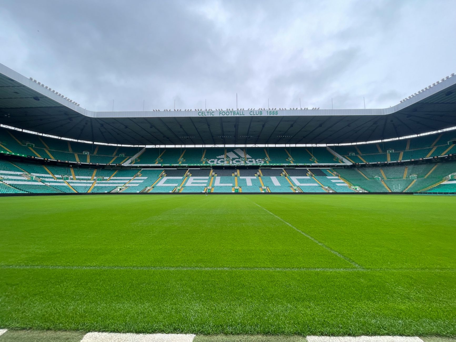 Wide-angle shot of the iconic Celtic Park stadium under a cloudy sky, showcasing its lush green field.