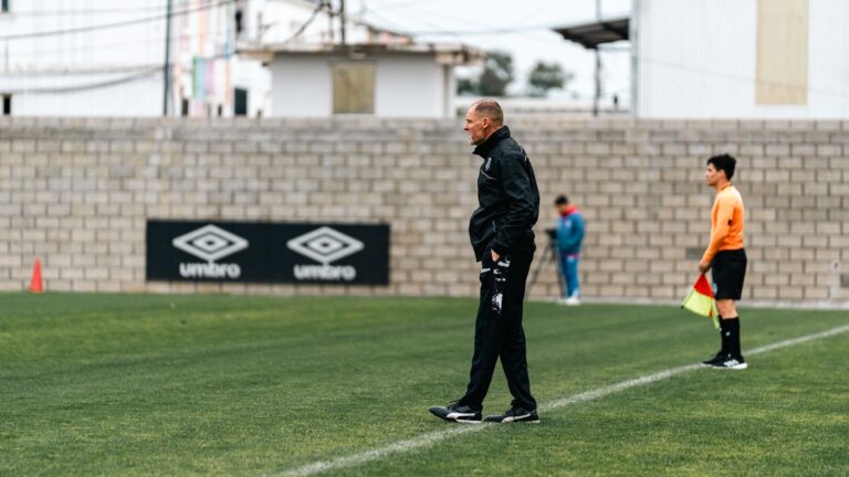 A soccer coach attentively observes a training session, standing by the sideline.
