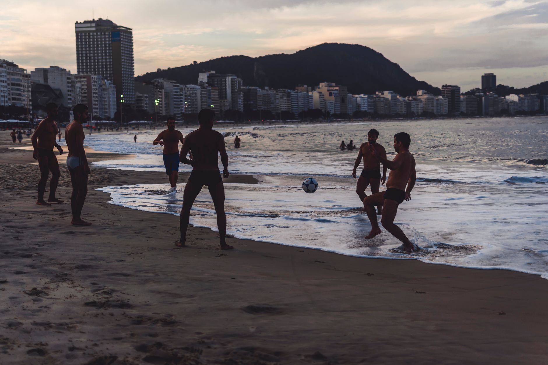 A group of friends playing soccer on Copacabana beach at sunset in Rio de Janeiro, Brazil.