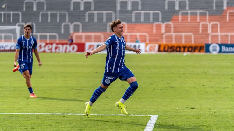 Two soccer players in blue uniforms celebrate a goal on the field.