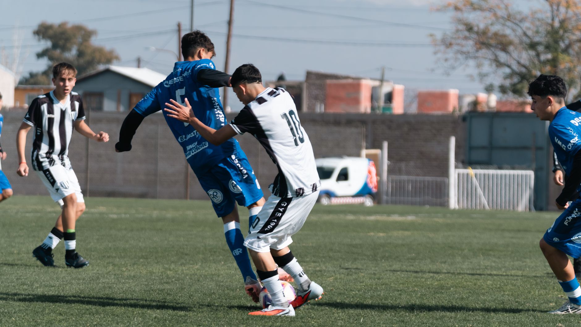 Intense soccer match between young players clad in blue and white uniforms on a sunny day.
