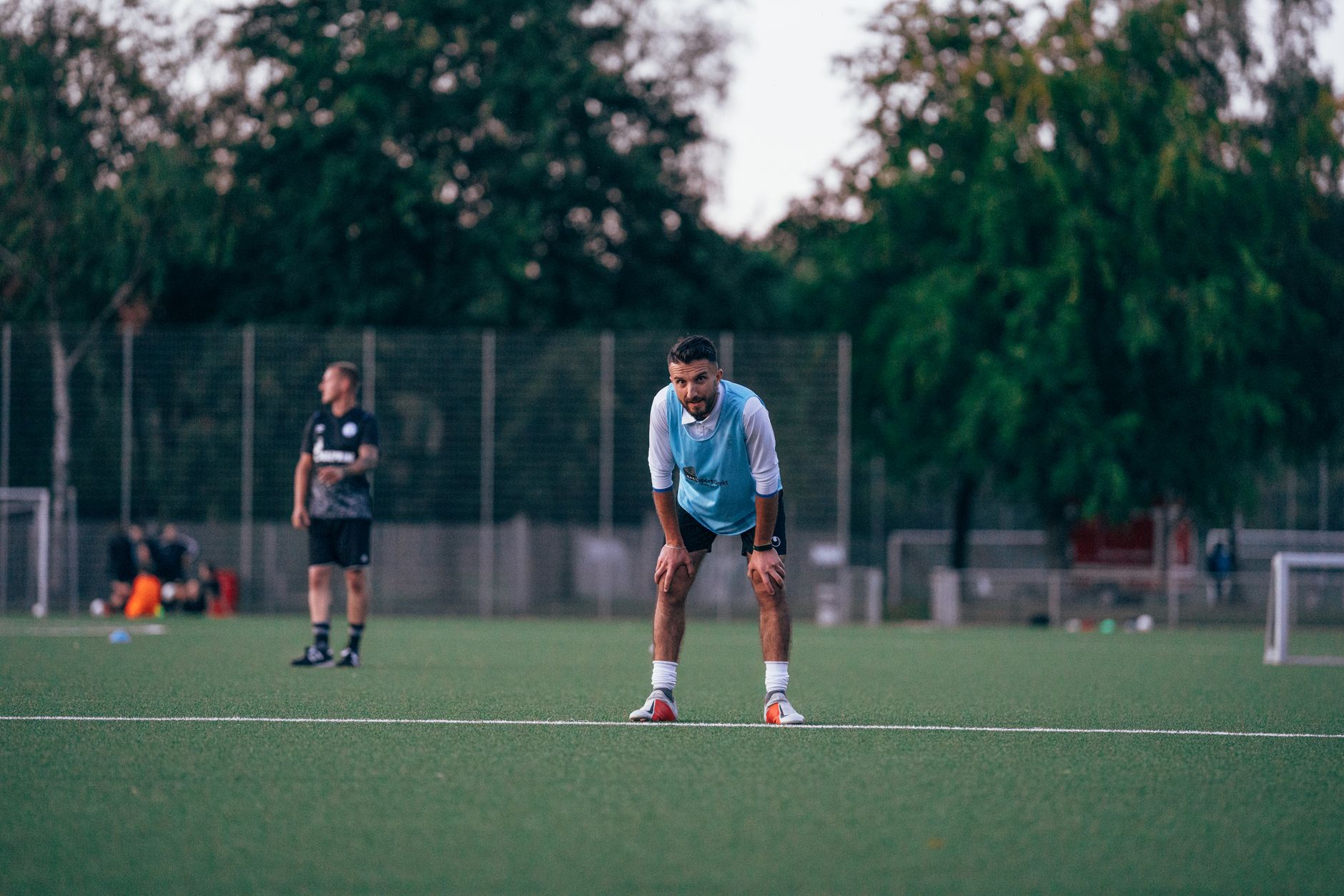 Male soccer player in uniform standing in field and leaning on hands during training in grassy field