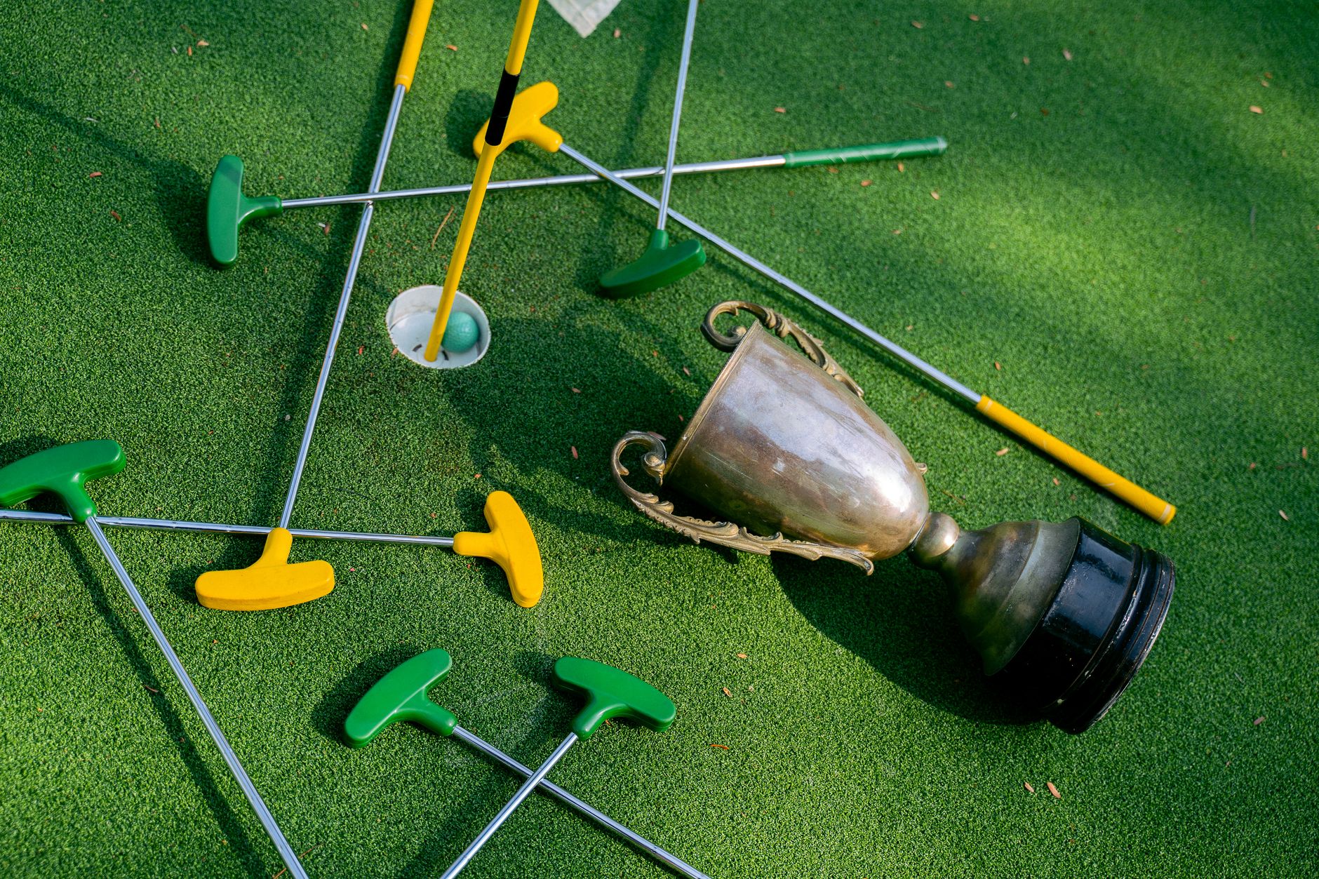 Colorful mini golf putters with a trophy on vibrant green turf, symbolizing victory.