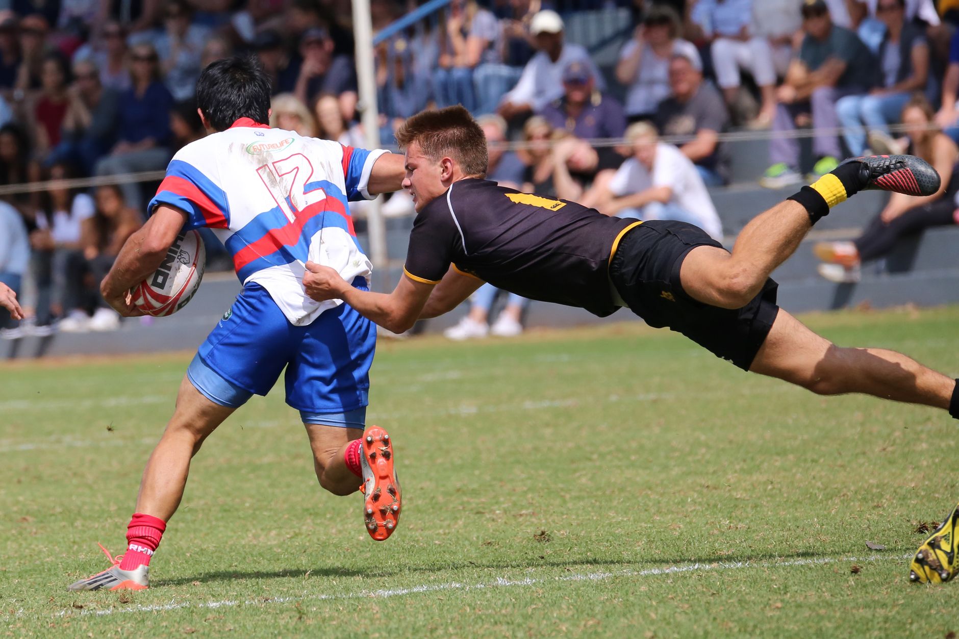 A thrilling rugby match capturing a player making a diving tackle on the field.