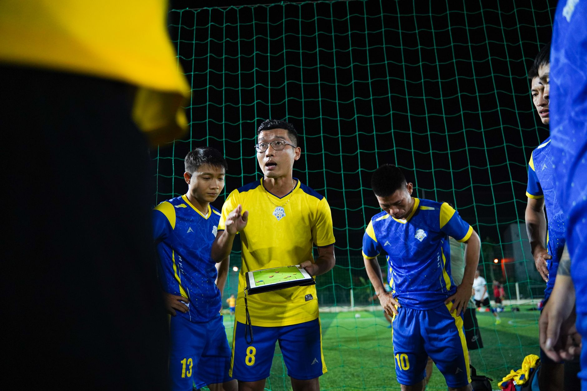 Soccer coach giving strategy talk to players on a night field.