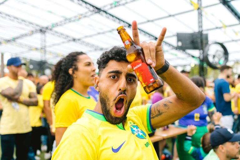 Energetic Brazilian fan with beer cheering for football team outdoors.