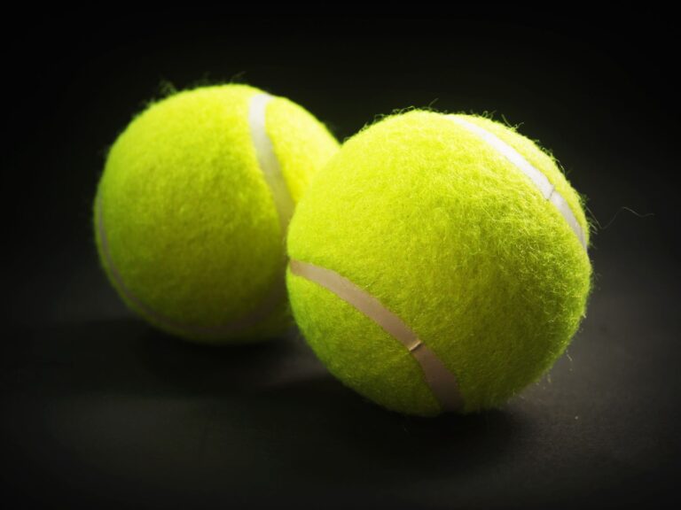 Close-up of two tennis balls with a vibrant yellow color on a dark background.