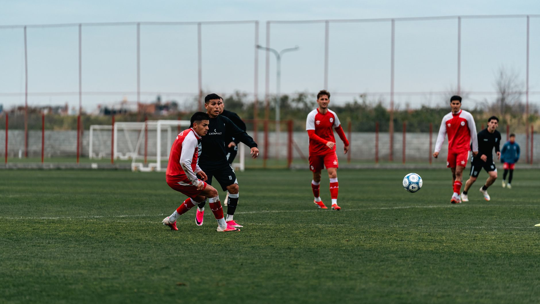 Dynamic soccer match with players in red uniforms during the day on a field.