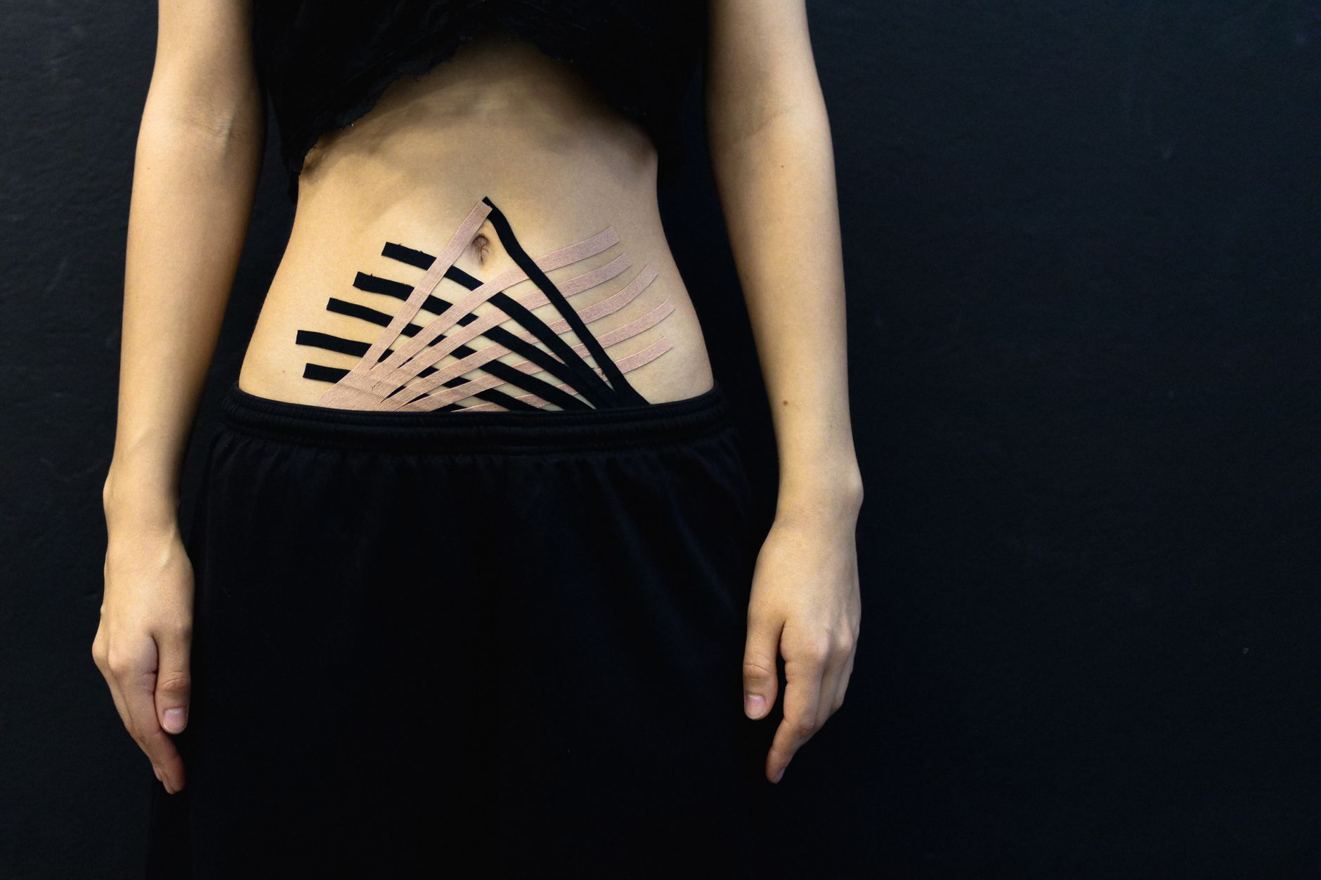 Female abdomen with kinesiology tape for physical therapy on black background.