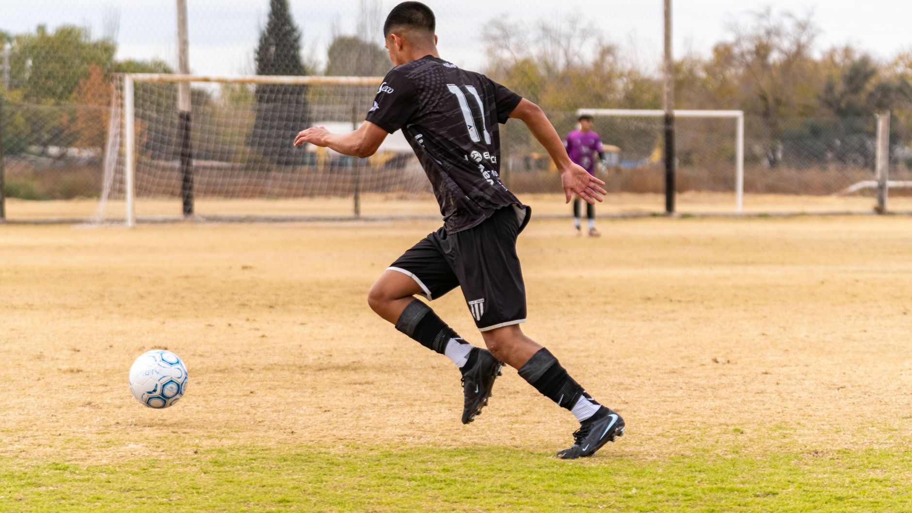 Soccer player dribbling the ball during a match on an outdoor field.