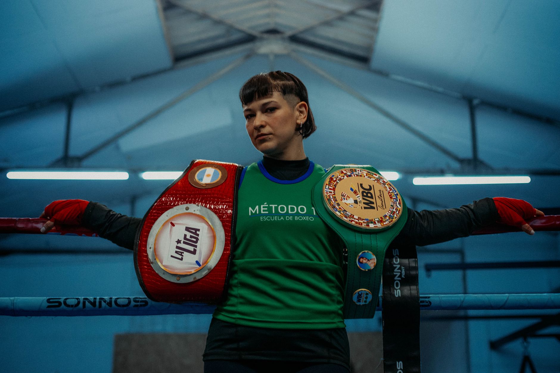 Female boxer poses with championship belts in an indoor boxing gym in Buenos Aires.