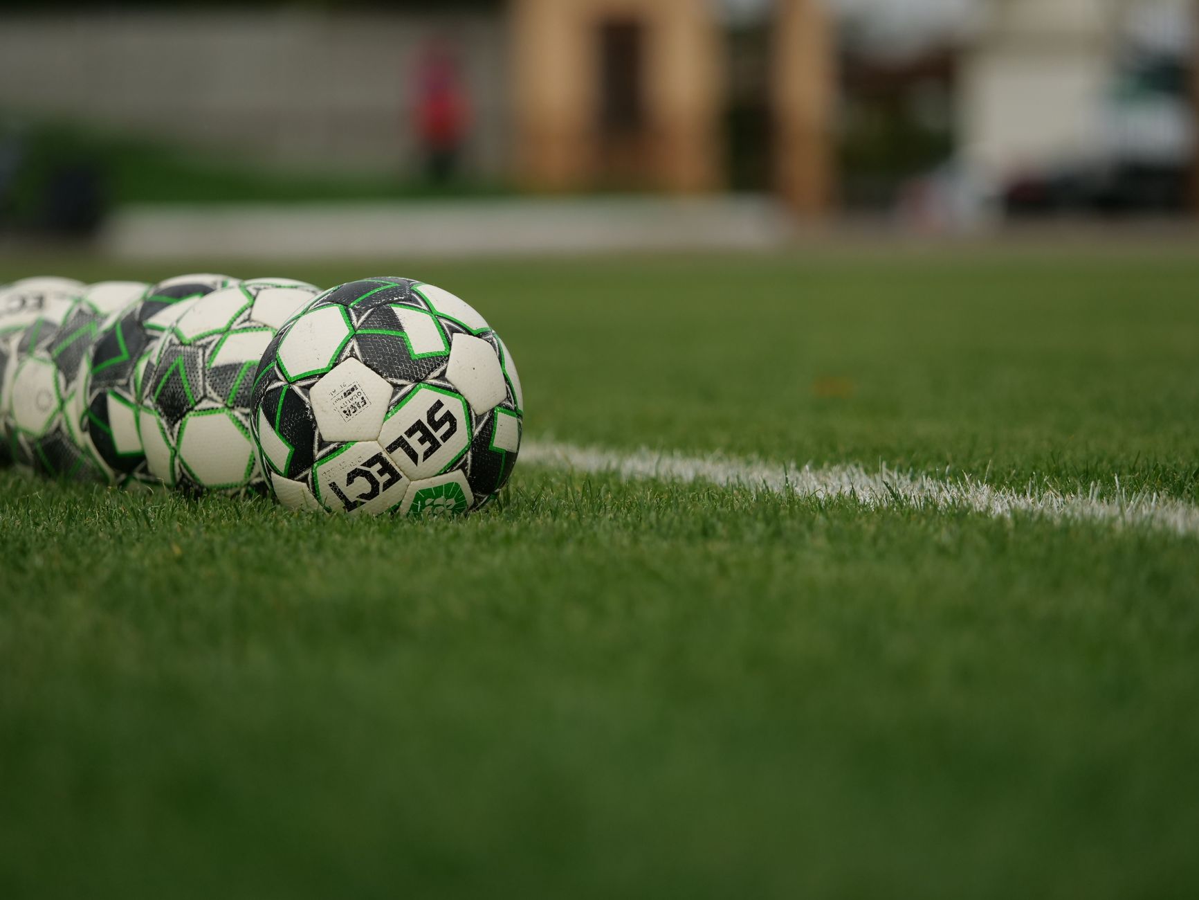 Close-up view of soccer balls lined up on a grassy football field.
