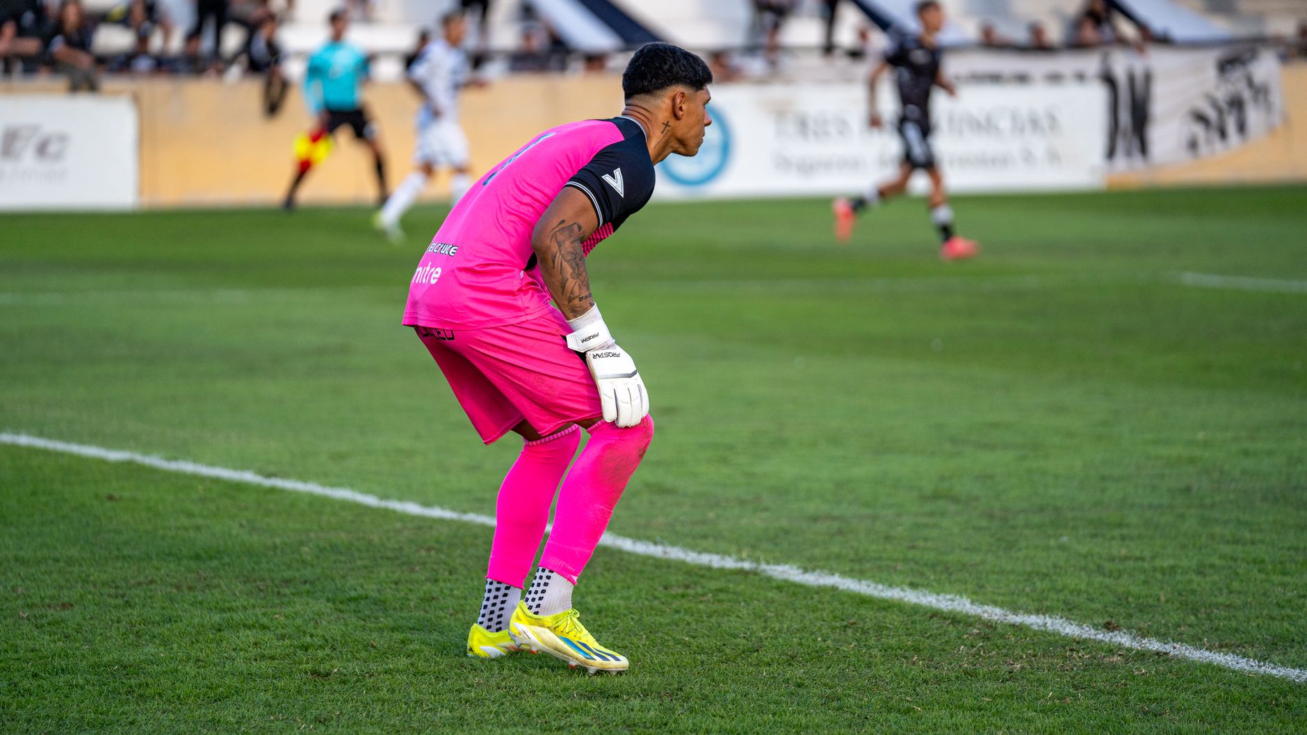 Soccer goalkeeper wearing pink kit in a match, showcasing focus and readiness.