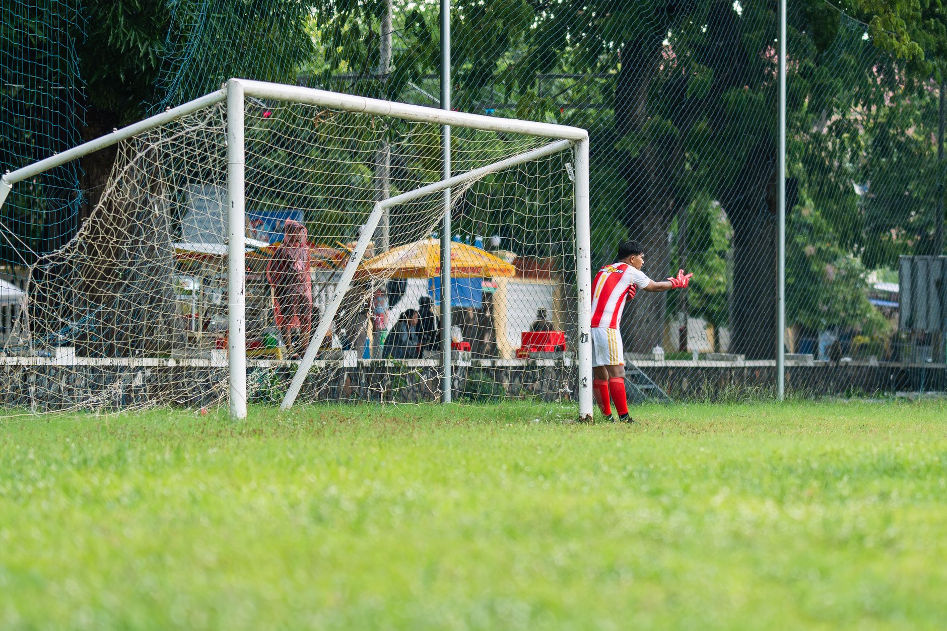 A young soccer player in action, defending the goal on an outdoor field during daytime.