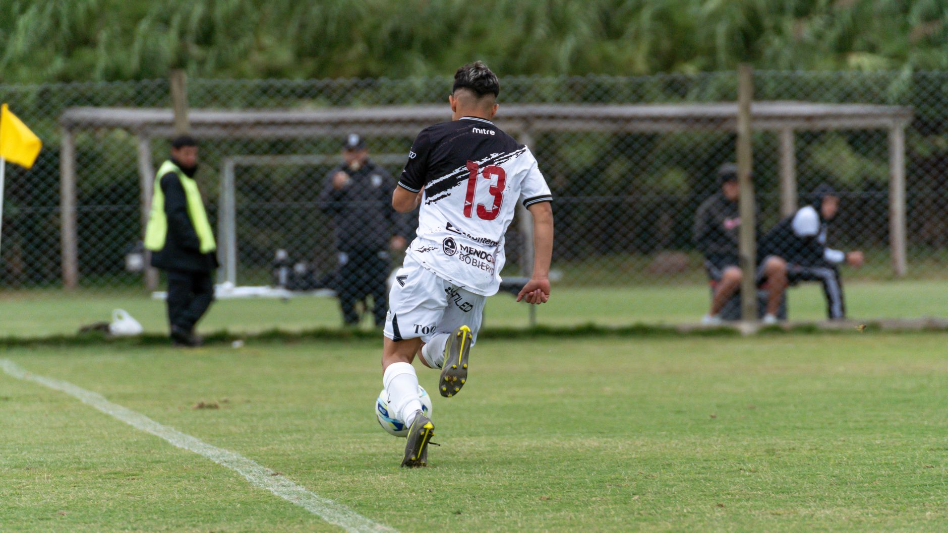 A teenager in soccer gear sprinting with the ball on a grassy field during a match.