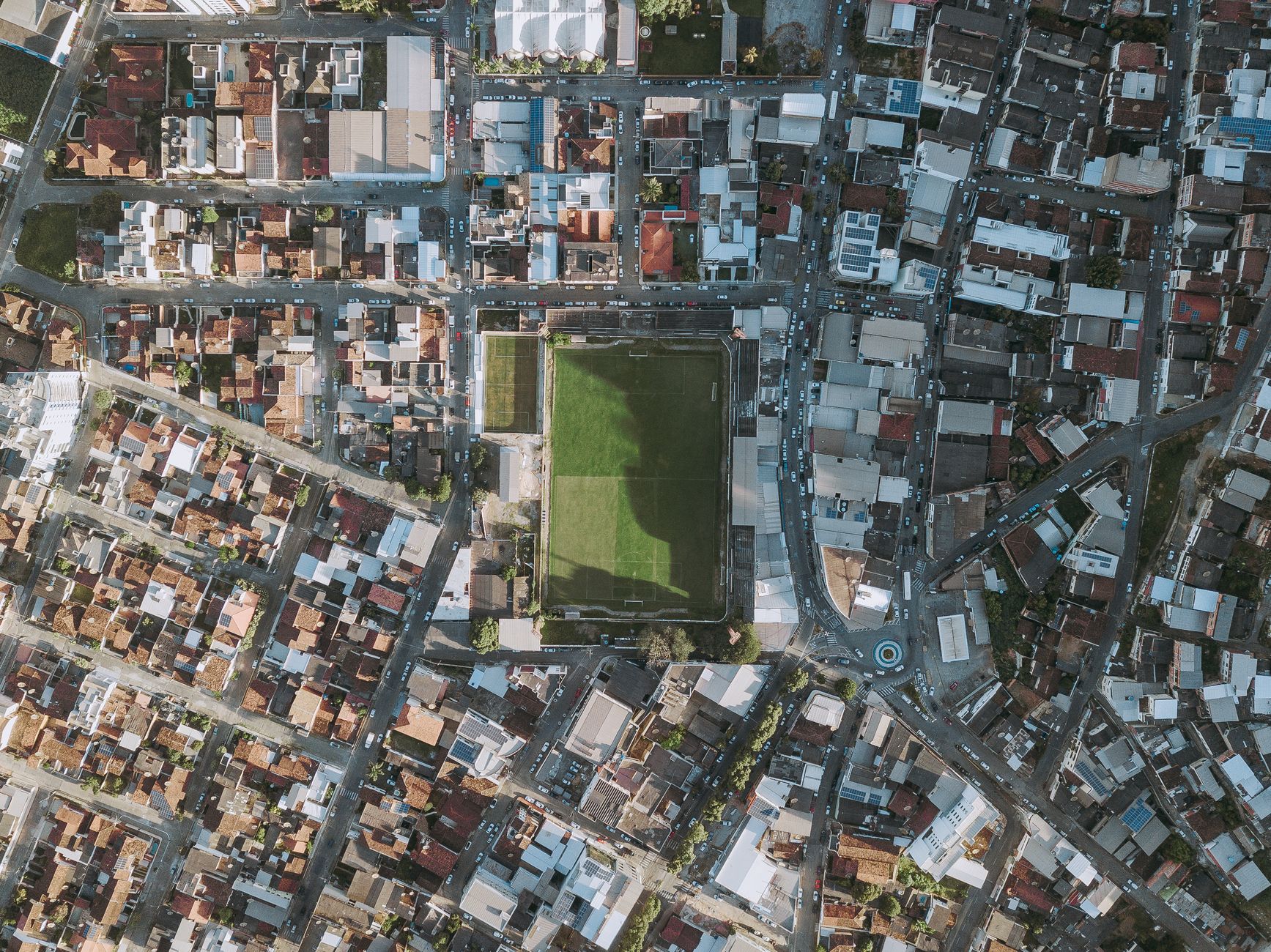 Aerial perspective of a soccer field amidst urban Coronel Fabriciano, showcasing vibrant city life.