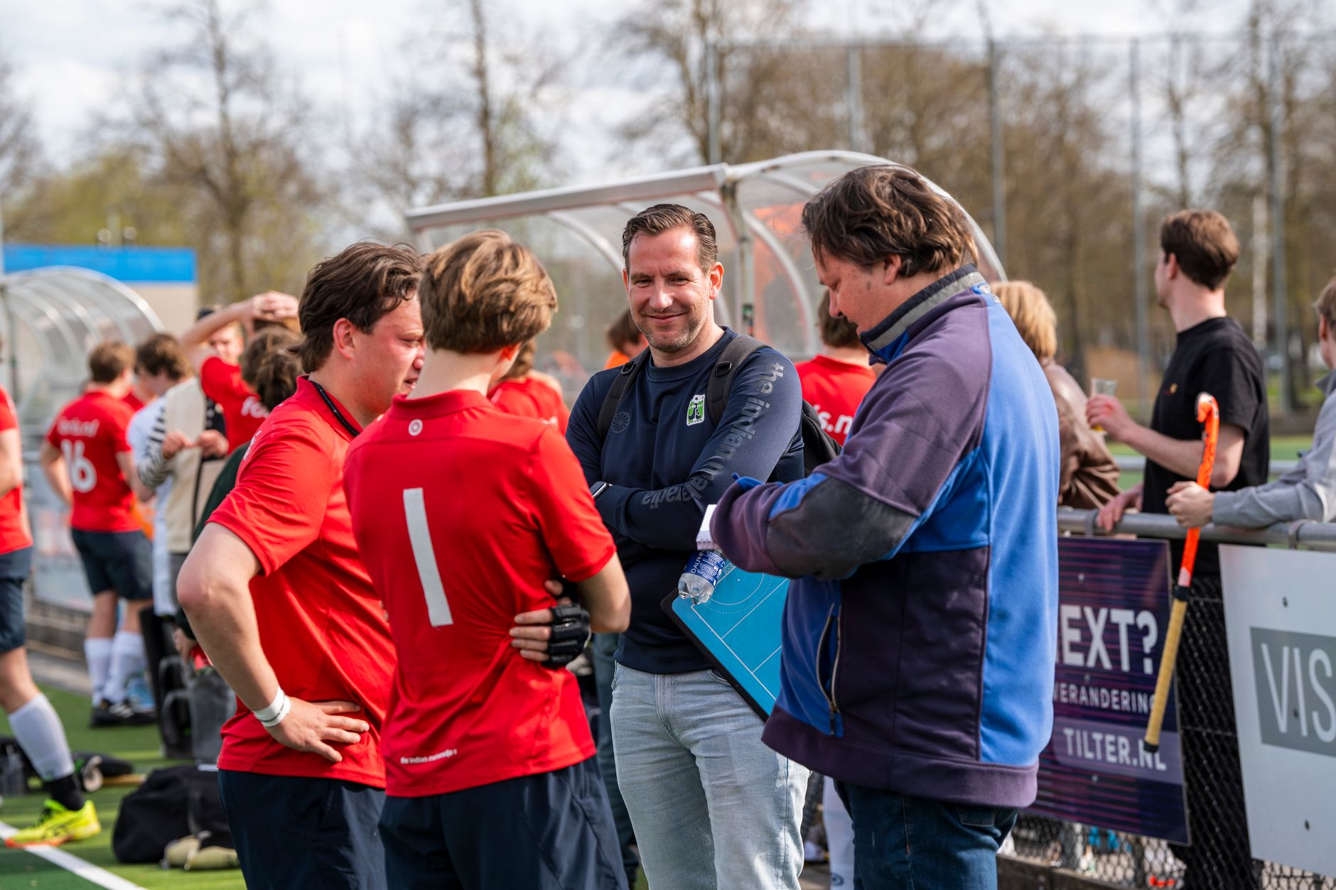 Field hockey players discussing strategy with coaches outdoors during a match.