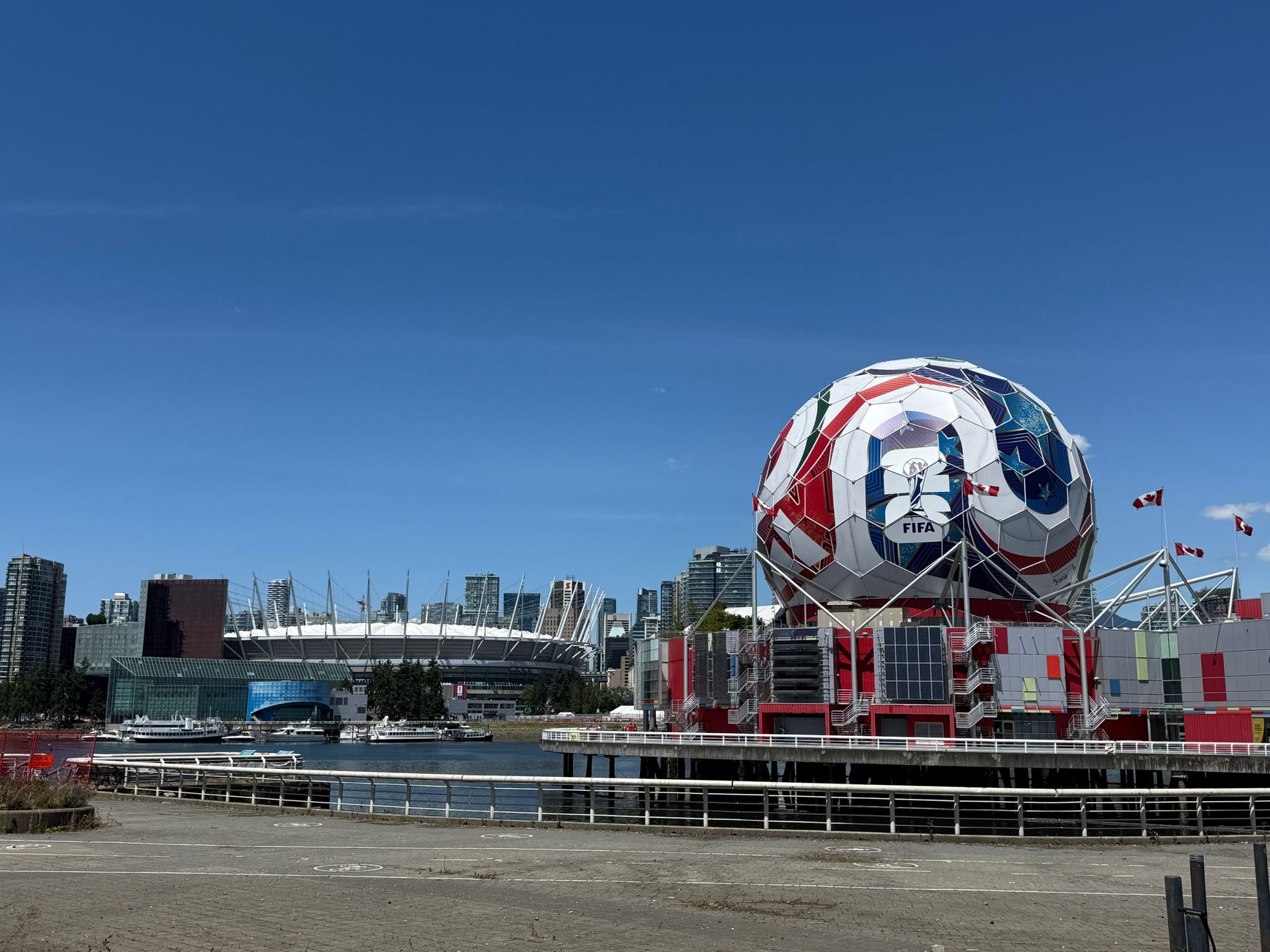 View of Vancouver's Science World featuring FIFA display and BC Place Stadium under a clear blue sky.