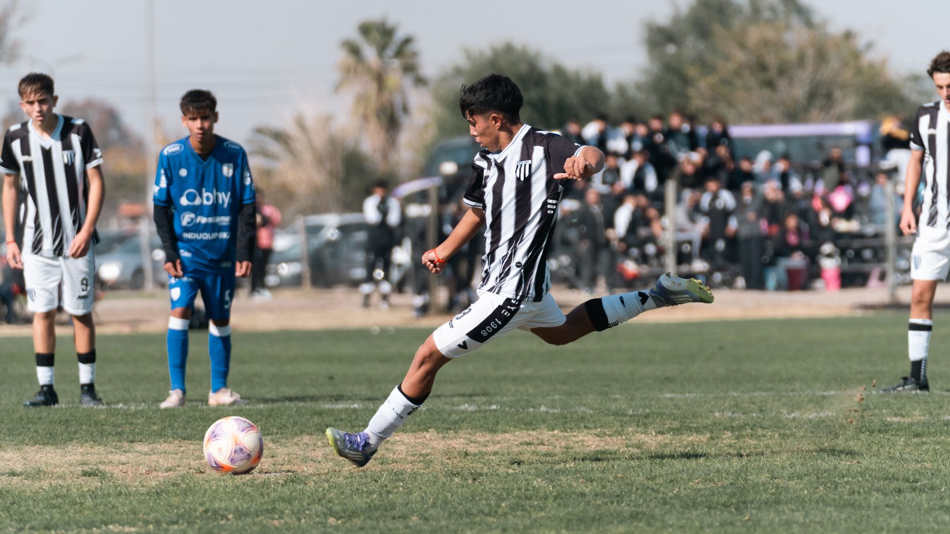 A young soccer player in action, taking a powerful kick during a competitive outdoor match.