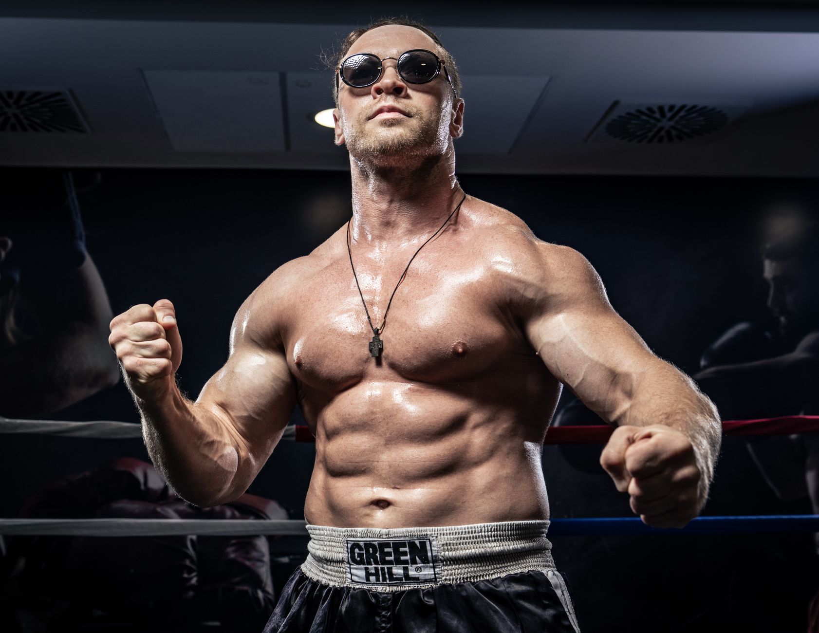 Powerful boxer in sunglasses posing confidently in a boxing ring, highlighting strength and fitness.
