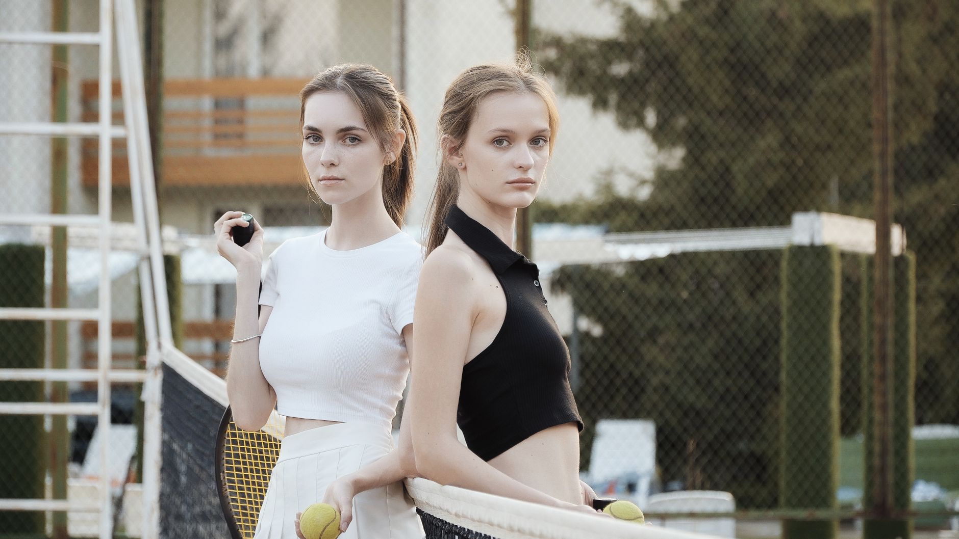 Two young women posing confidently on a tennis court, showcasing a summer sports fashion look.