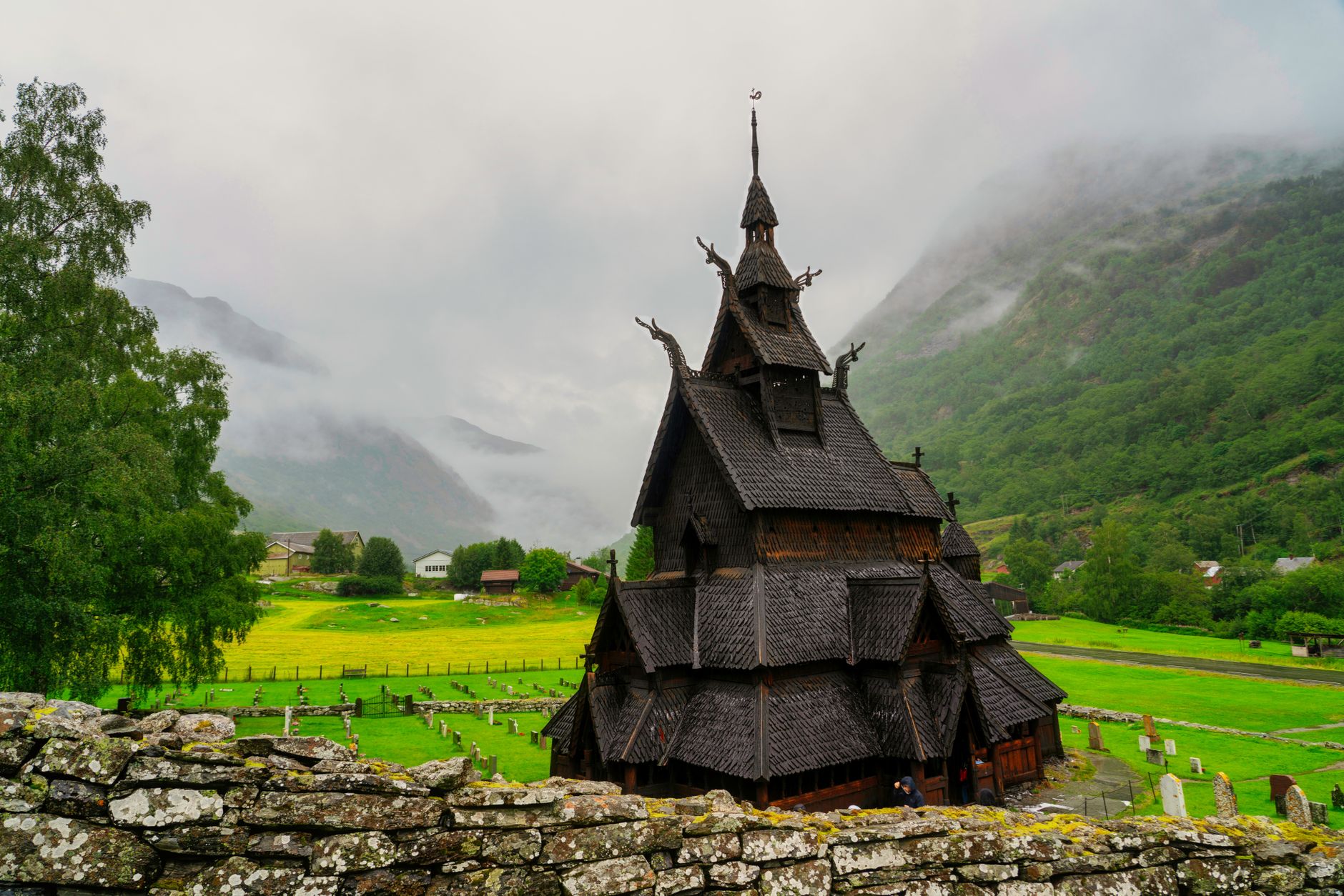 Borgund Stave Church with misty mountains and lush greenery in Vestland, Norway.