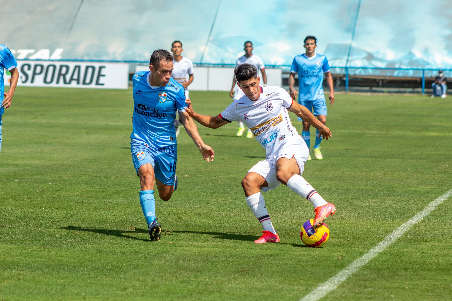 Soccer players compete fiercely during a daytime match on a grassy field.
