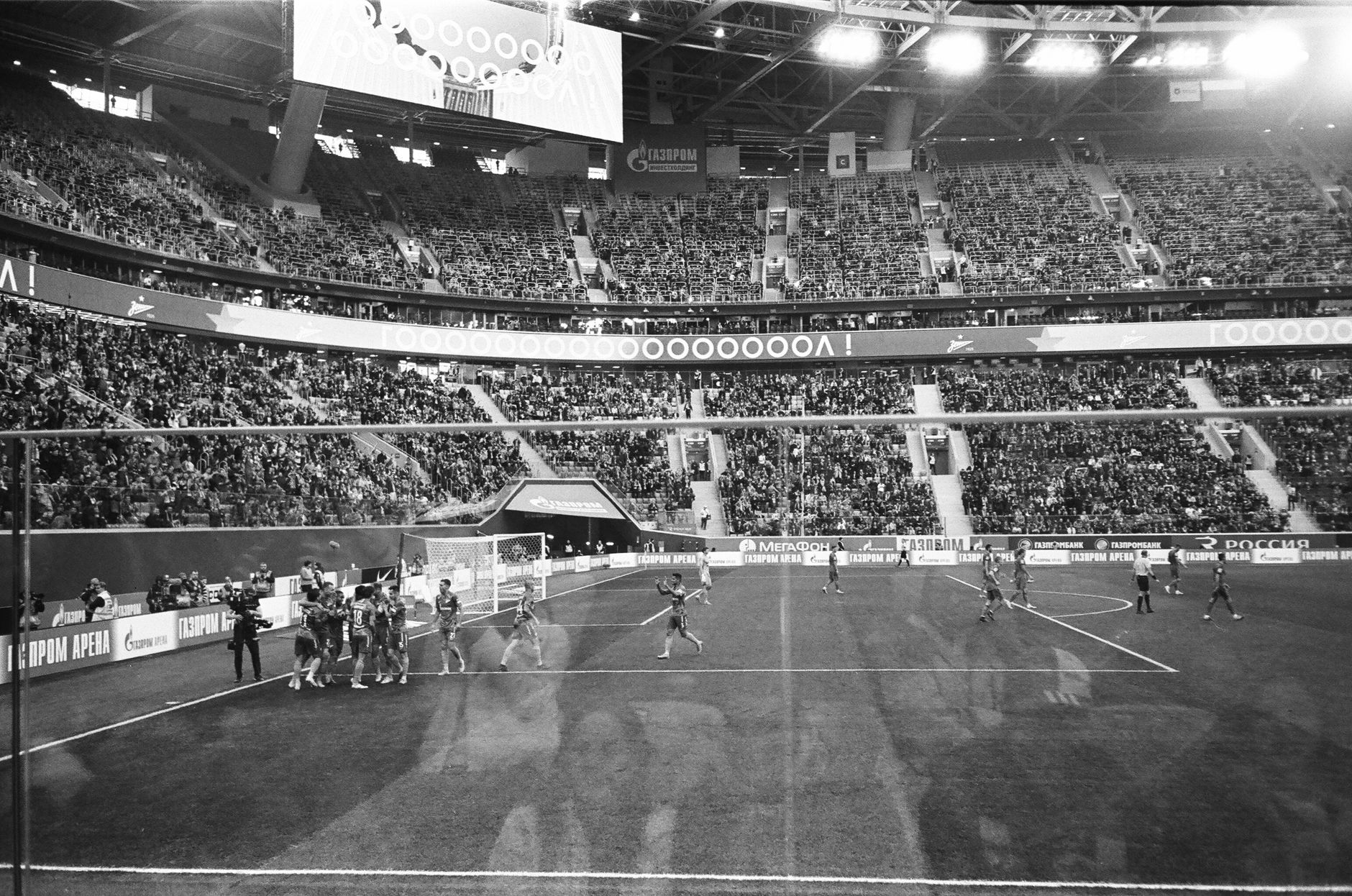 Through glass black and white football team standing together and congratulating each other with match win game in crowded stadium