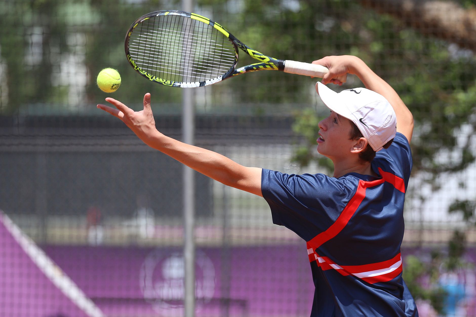 Teenage tennis player in action serving on a sunny outdoor court.