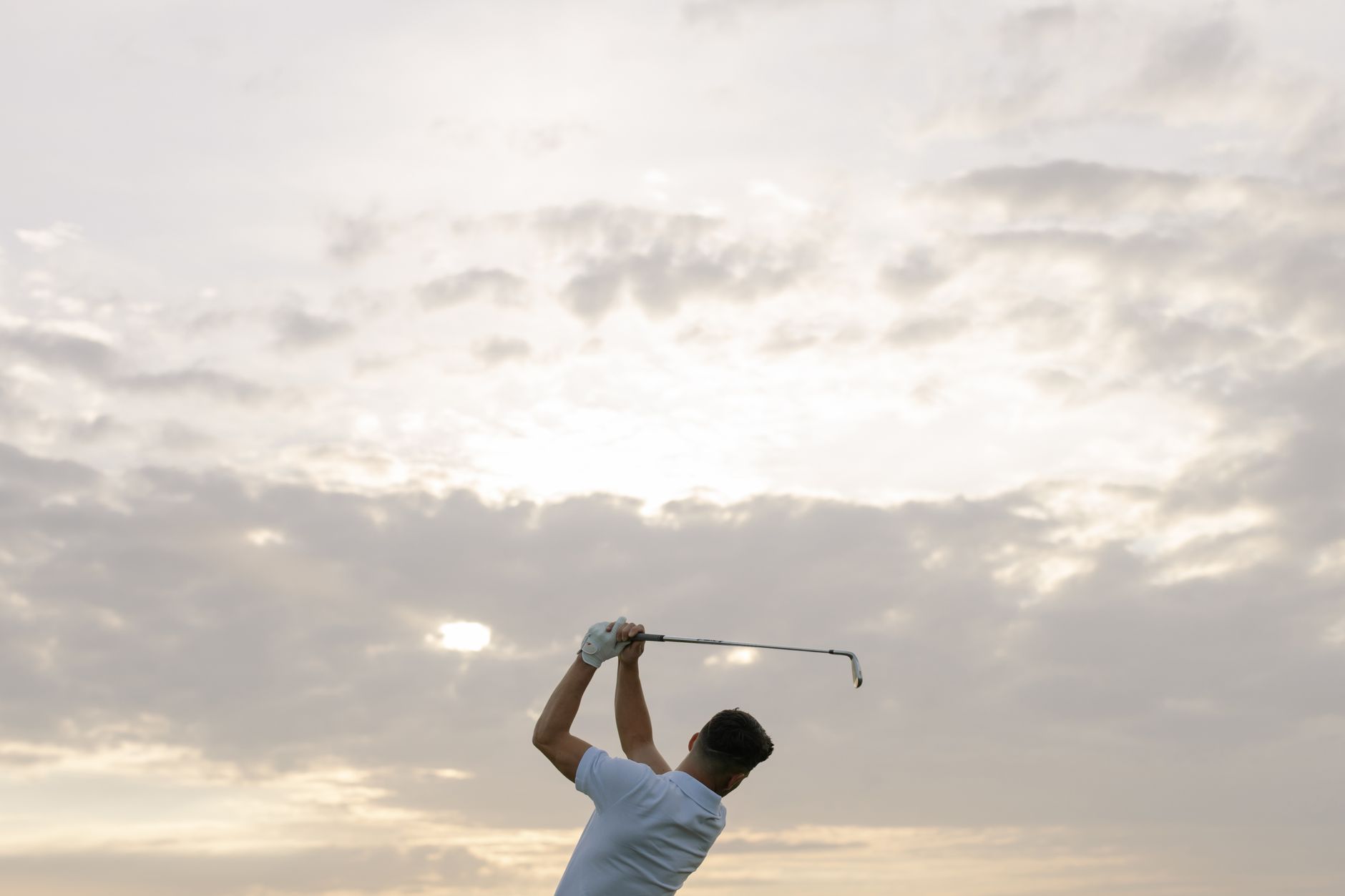 A golfer swings his club against a dramatic cloudy sky, capturing the essence of the sport.