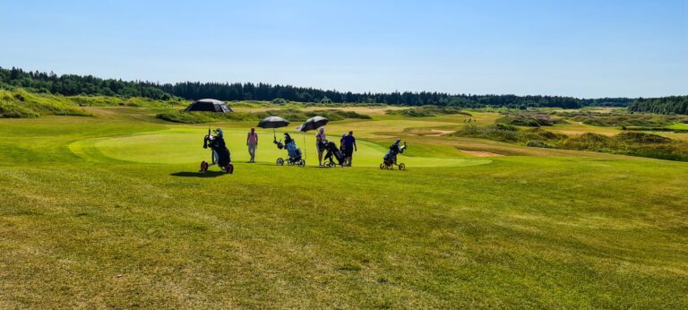 Scenic view of golfers on a lush green golf course under clear blue skies.