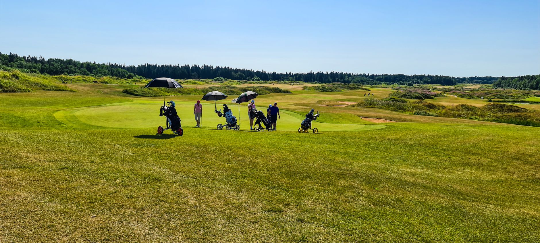 Scenic view of golfers on a lush green golf course under clear blue skies.