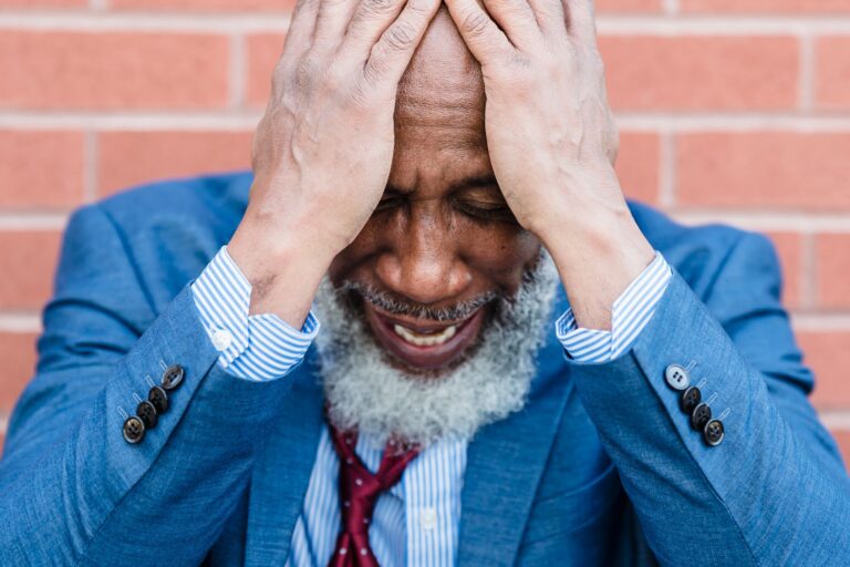 Close-up of a stressed African American man with a beard holding his head, expressing anxiety.