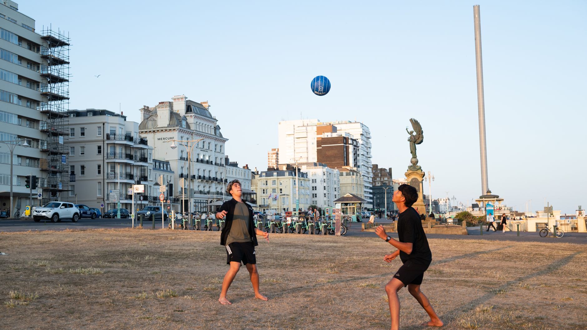 Two teenagers play football on a sunny summer day by Brighton's iconic seaside promenade.