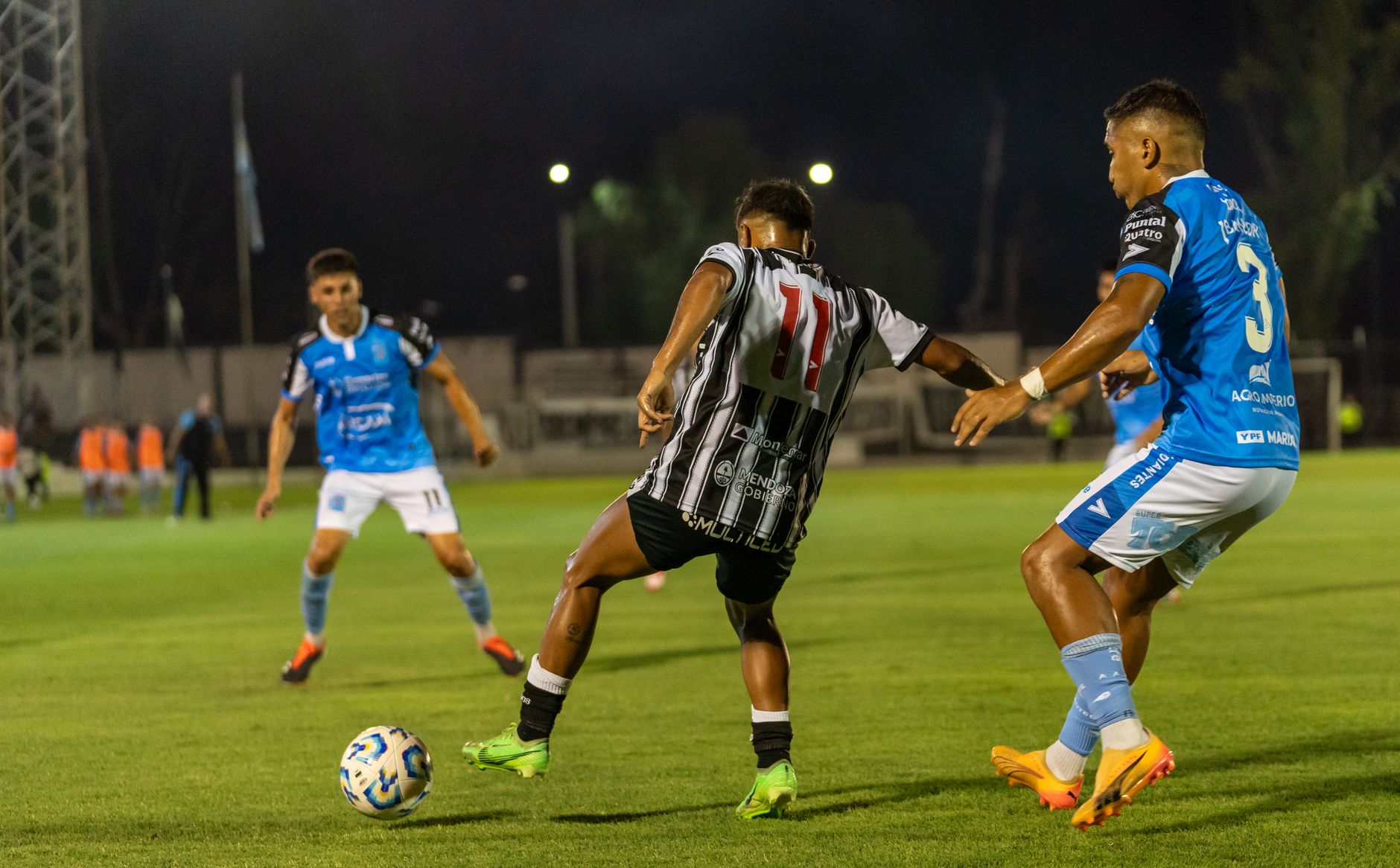 Players engage in a competitive football match at night under bright stadium lights.