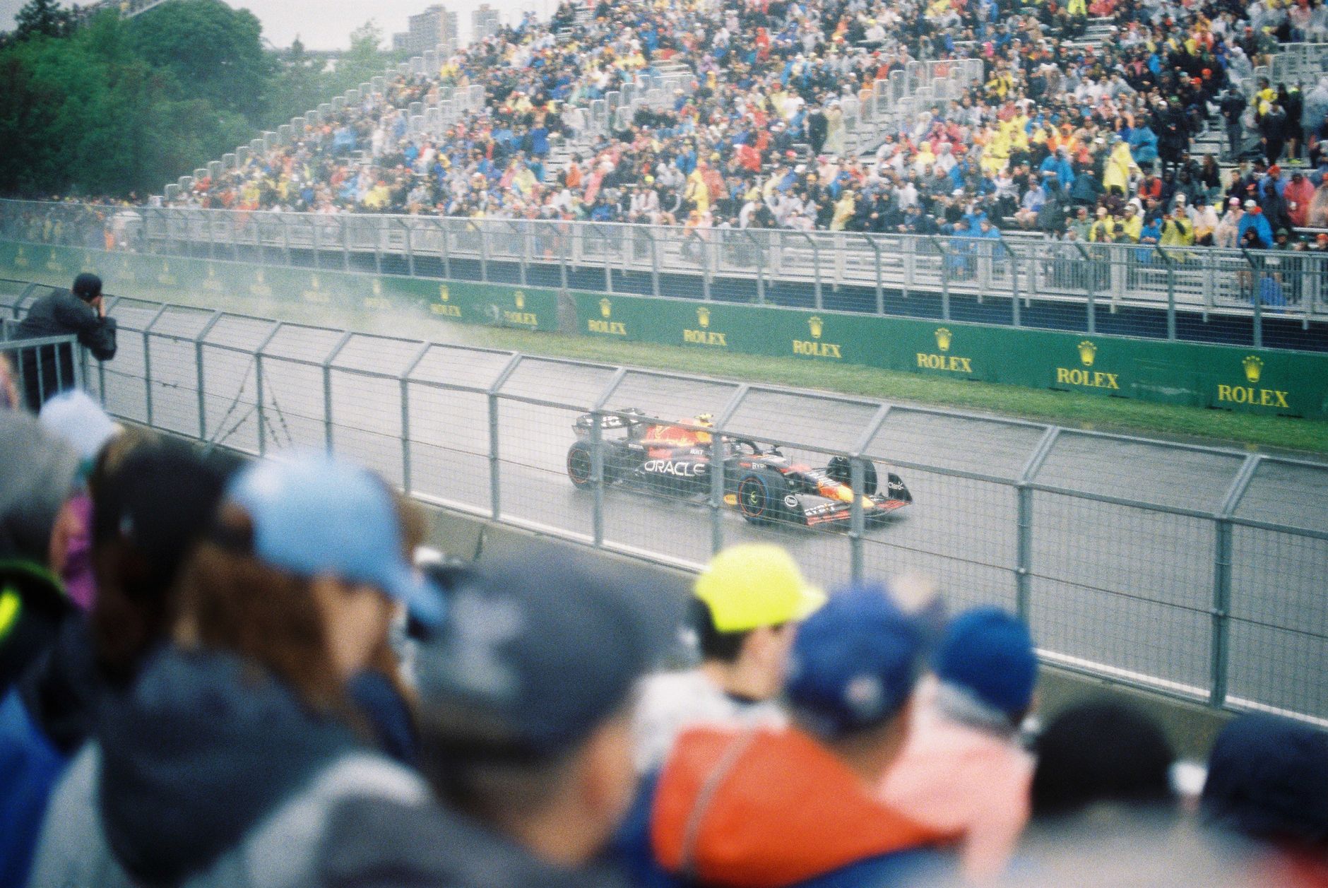 High-speed Formula One car racing on a wet track with a packed crowd of spectators.
