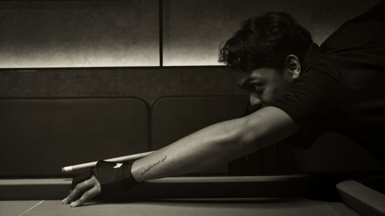 A focused billiard player with tattoo lining up a shot on a pool table indoors.