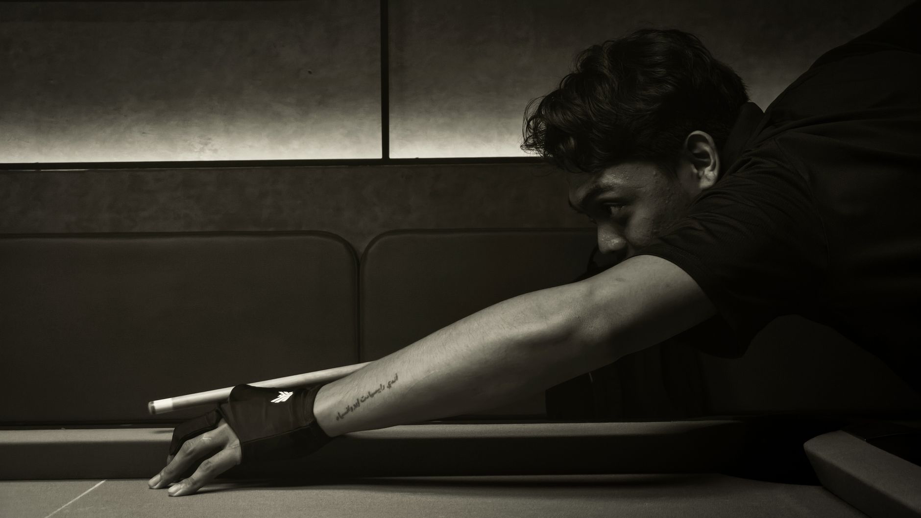 A focused billiard player with tattoo lining up a shot on a pool table indoors.