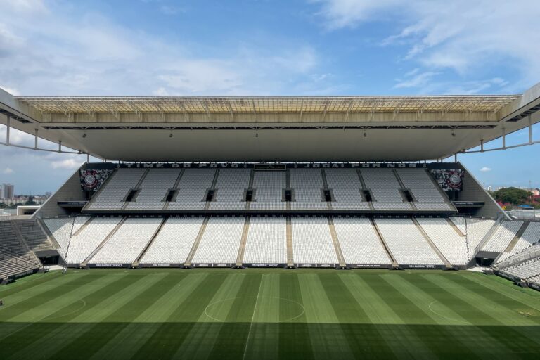 Wide view of an empty football arena in São Paulo, featuring a green pitch under a sunny sky.