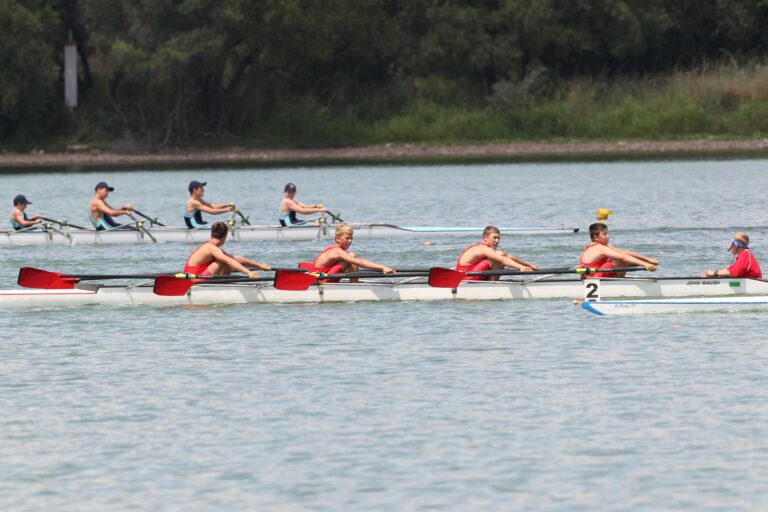 Two rowing teams race on a scenic lake, showcasing teamwork and athletic skill.