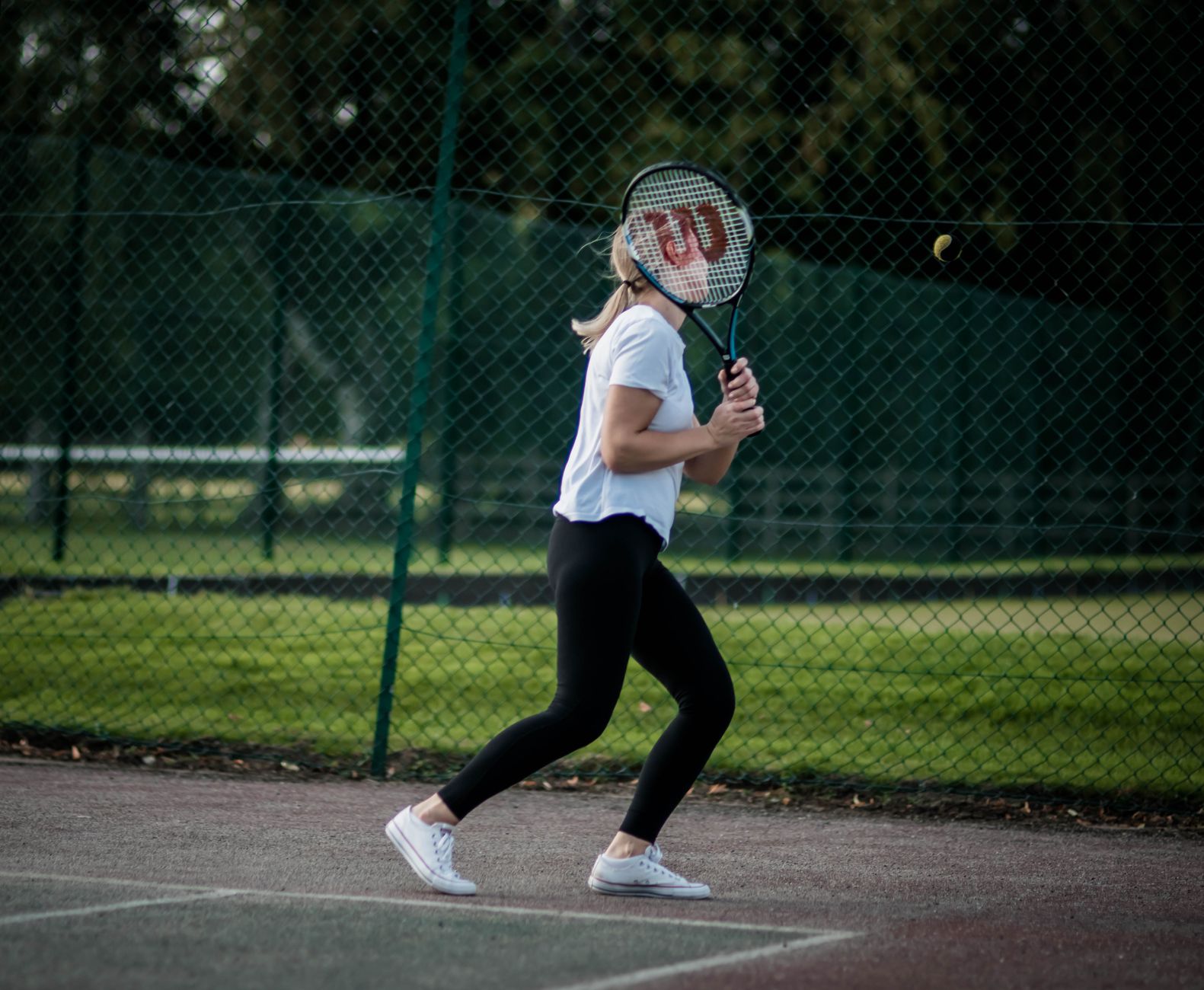A woman playing tennis outdoors, poised with her racket for a return shot on a sunny day.