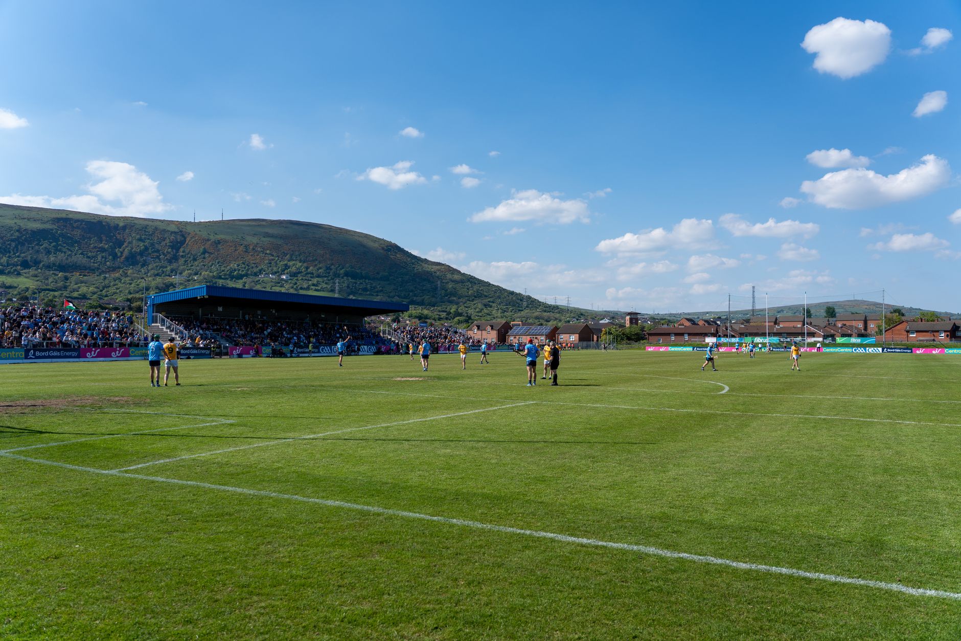 A lively Gaelic football match under blue skies with scenic hills in Ireland.