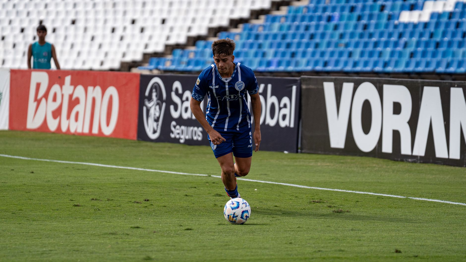 A soccer player in blue and white uniform dribbling a ball on a grass field during a match.